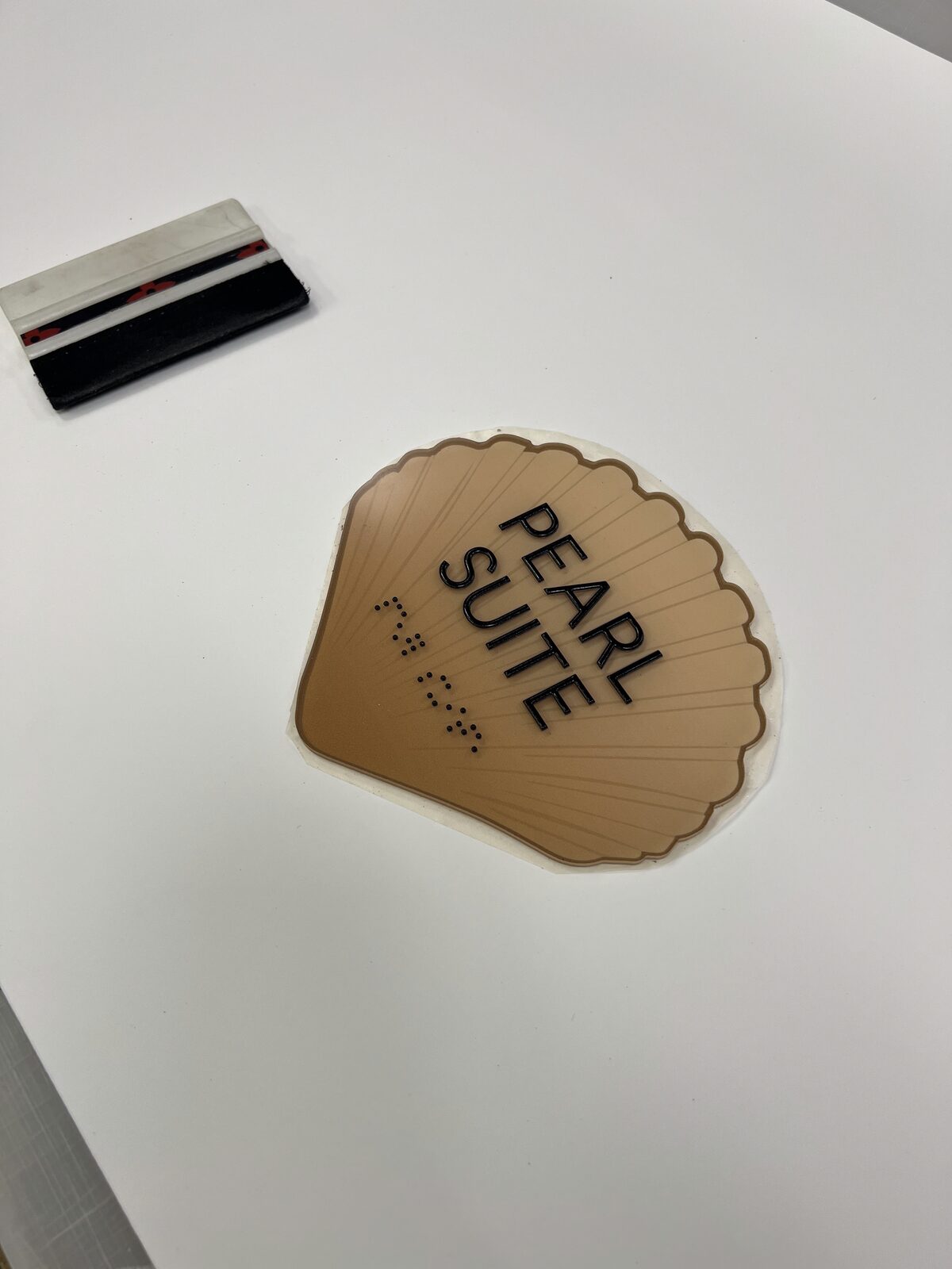 A shell-shaped Pearl Suite room plaque with tactile copy and Braille by Studio OntheRock