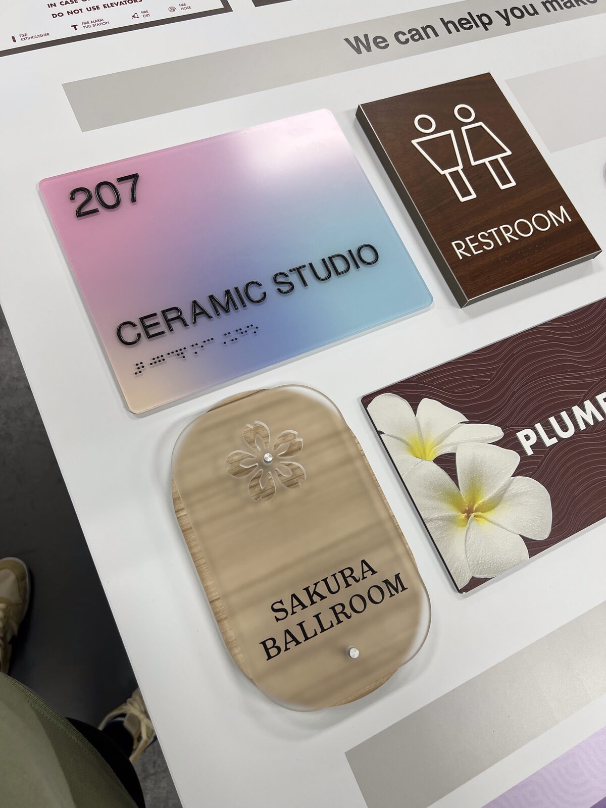 A grouped collection of ADA room-ID and restroom plaques by Studio OntheRock, with tactile copy, Braille, and decorative gradient and wood-tone finishes